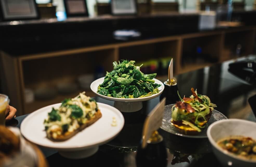 Three plates of food, one open faced sandwich with chicken and spinage, one tall leafy salad and one baked potato with leafy greens on top.